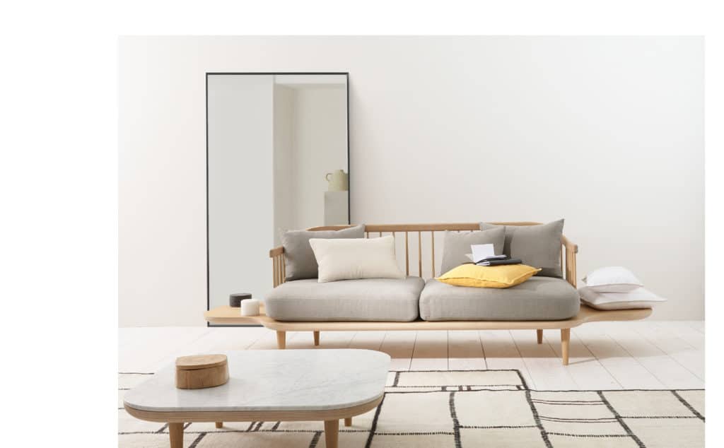 Soggiorno in stile minimal con divano a due posti con struttura in lengo chiaro, tavolino in marmo, grande specchio e tappeto a decoro geometrico.