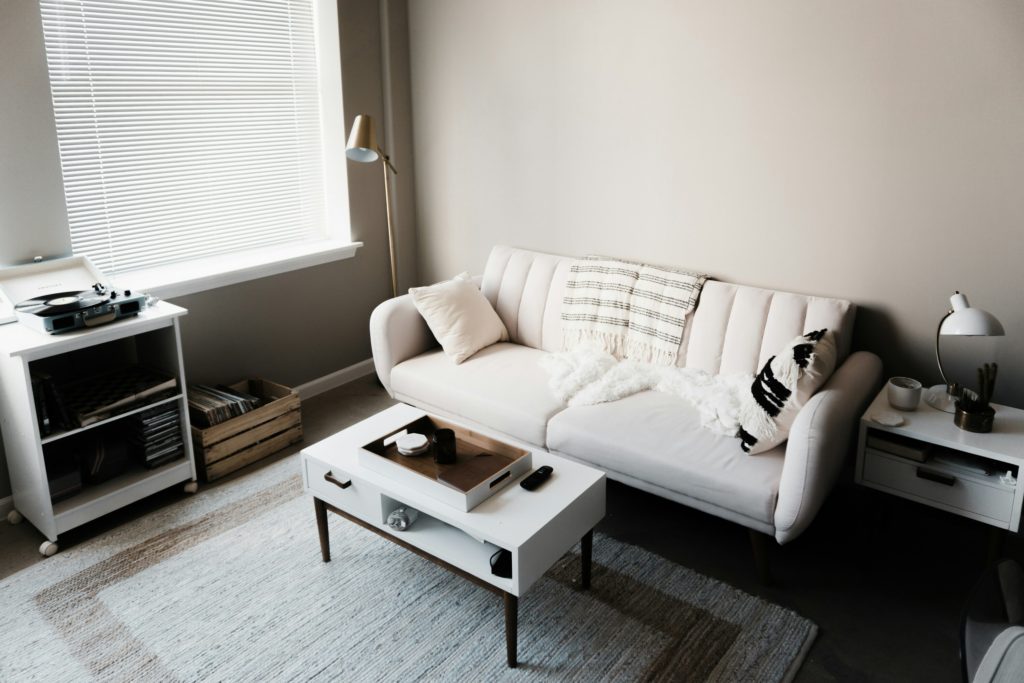 Vista dall'alto di un divano a tre posti bianco con tavolini da caffé laccati bianchi, tappeto in tessuto naturali chiaro e mobile porta giradischi.