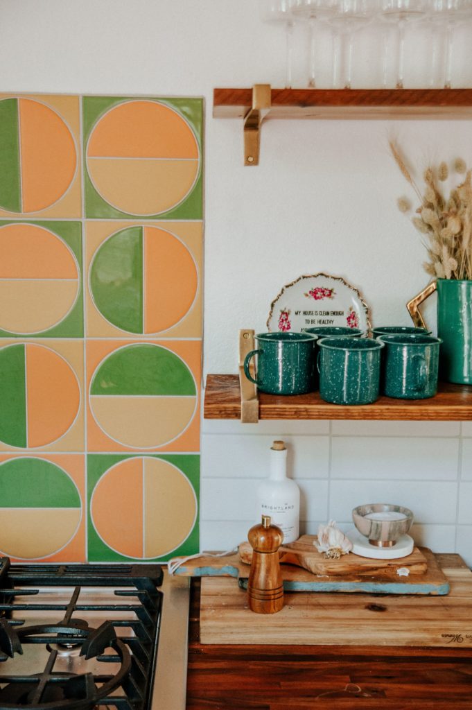 dettaglio paraschizzi cucina con piastrelle verdi e arancioni e tazze blu su una mensola 