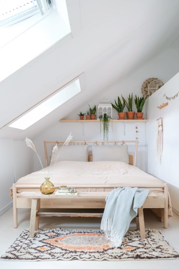 camera da letto in mansarda con tetto e pareti bianche e letto in legno chiaro