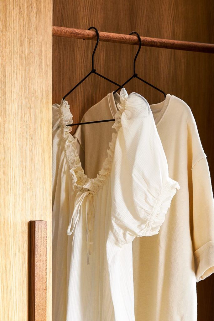 Vestiti bianchi appesi su tubo appendi abiti in legno all'interno di armadio in legno