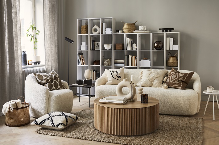 soggiorno in colori neutri con divano tessile bianco e poltrona a fianco. tavolo basso in legno di bambù e libreria bianca sul fondo