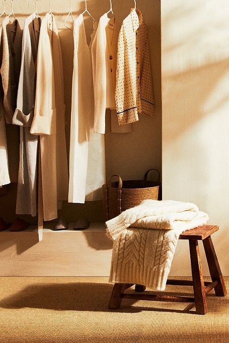 dettaglio di cabina armadio con vestiti appesi e sgabello in legno