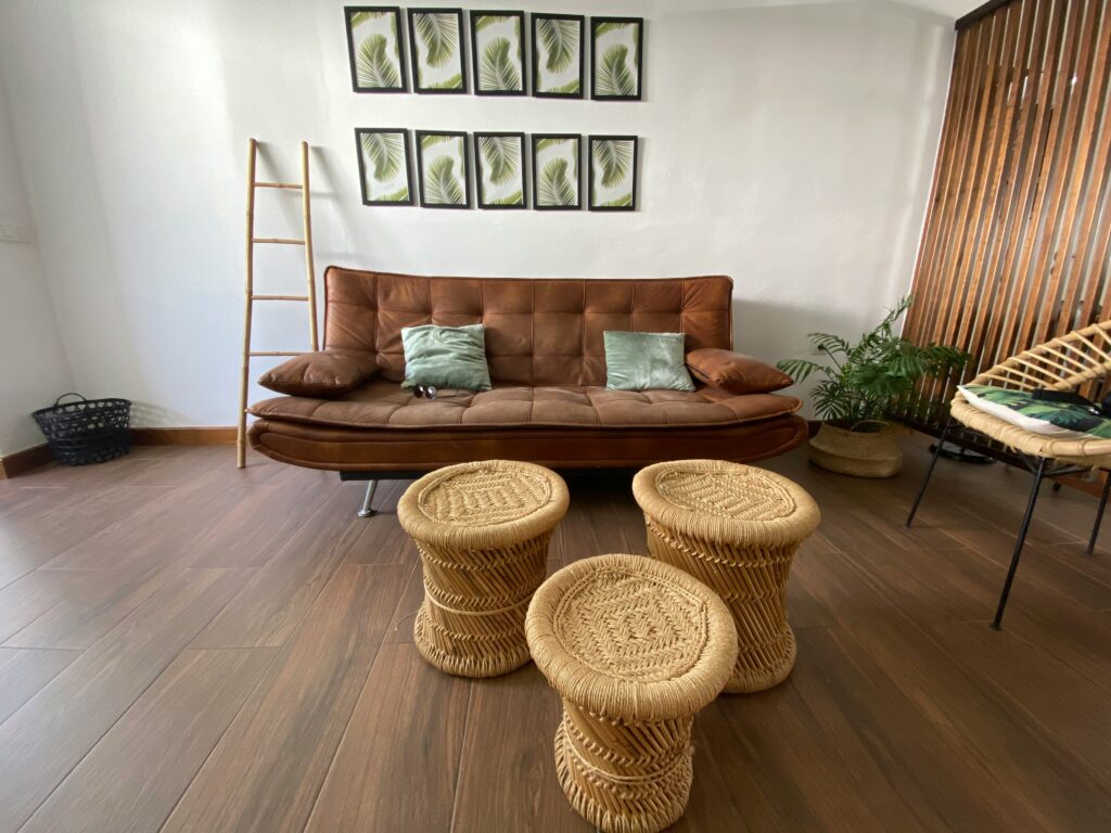 soggiorno boho-chic con divano in pelle, tavolini e sedia in vimini e pavimento in gres effetto legno.