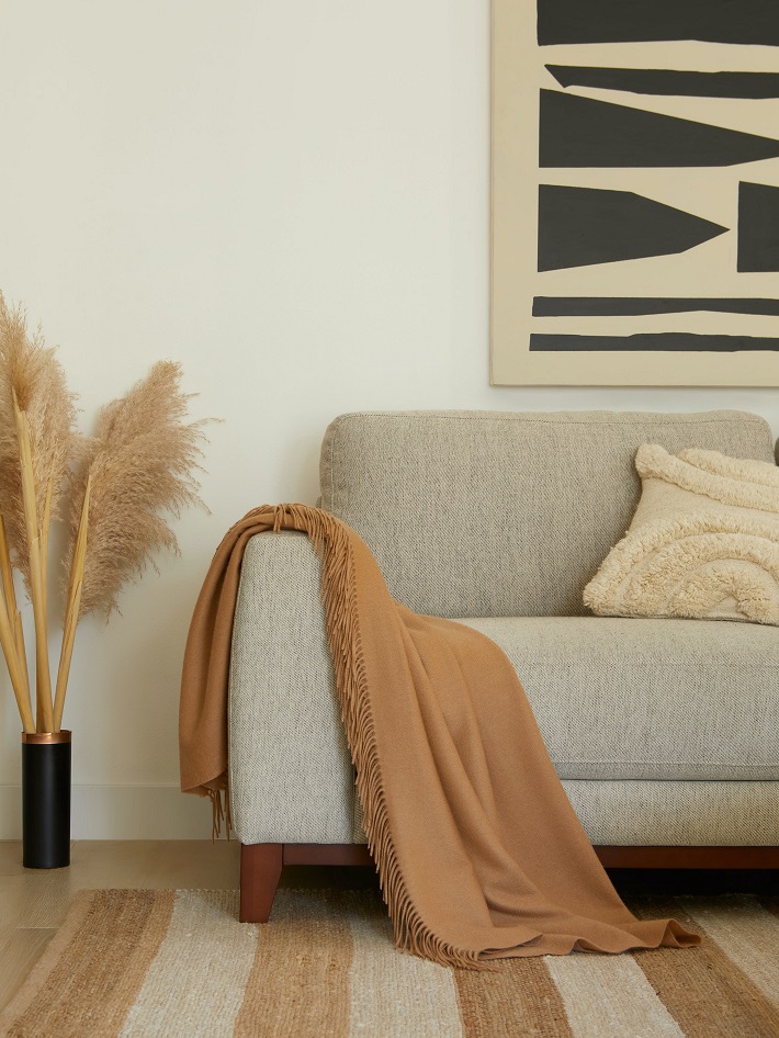 Materiali ecosostenibili per il design in un soggiorno con divano grigio, tappeto a righe ed erba pampa.