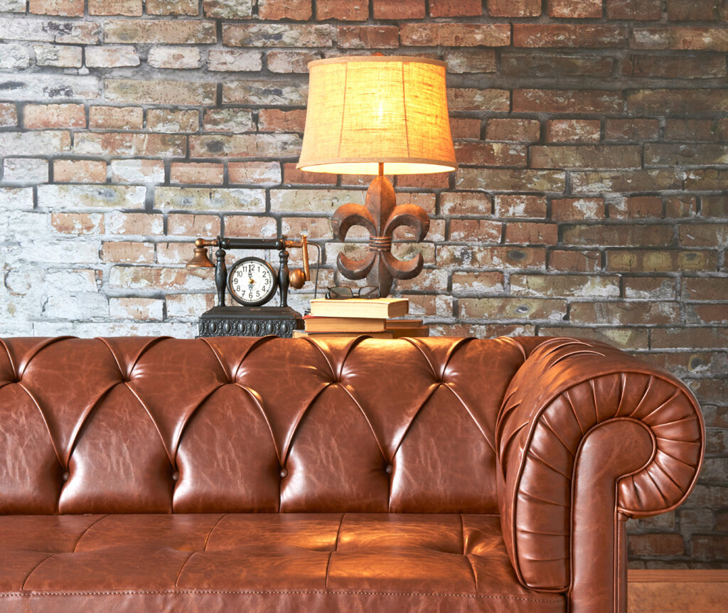 Divano Chesterfiled in cuoio marrone in soggiorno in stile industriale con parete di mattoni